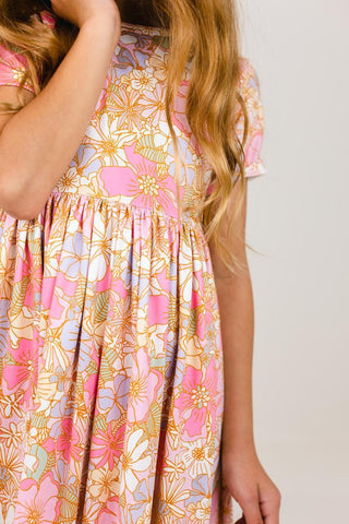 Girl wearing a floral dress with pink, yellow, and blue flowers on a plain background