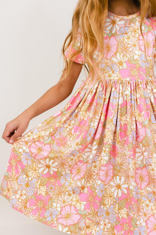 Child wearing a floral dress with pink and yellow flowers on a plain background