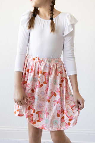Child wearing a white leotard and patterned skirt against a plain background