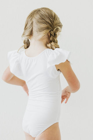 Child wearing a white leotard with ruffled sleeves on a plain background