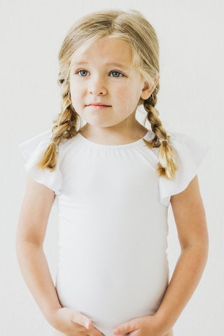 Young girl with braided hair wearing a white leotard against a plain background