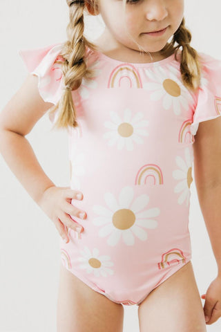 Child wearing a pink leotard with rainbow and flower patterns on a white background