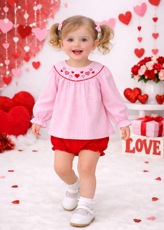 Child in pink bloomer set with red accents standing in a Valentine's Day decorated room.