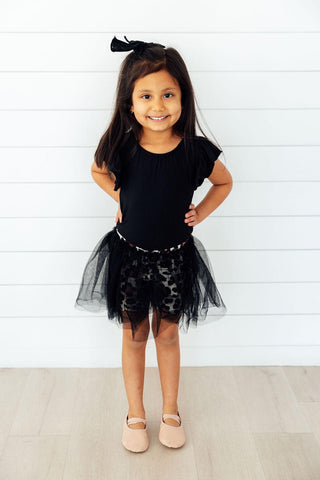 Young girl wearing a black leotard and leopard print tutu skirt against a white background