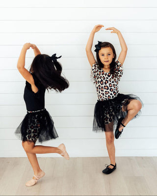 Two young girls in dance poses wearing leopard print tops and black tutus against a white background.