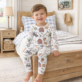 Child wearing pajamas with farm-themed design sitting on a bed in a bedroom.